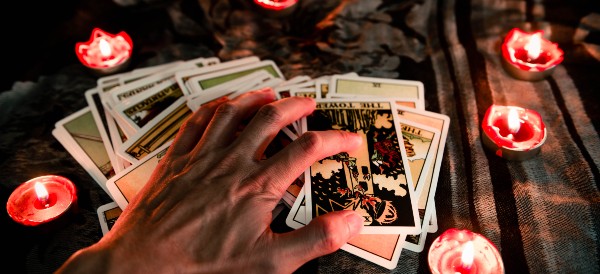 a hand spreading out tarot cards with tealight candles around them
