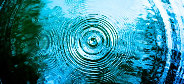 a single rain drop falling into a lake, creating ripples