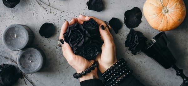 a woman holding a handful of black roses on a grey table, with candles and more flowers around her