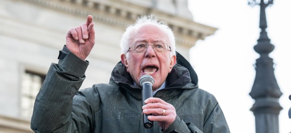 bernie sanders speaking and gesturing into a mic while wearing a heavy coat