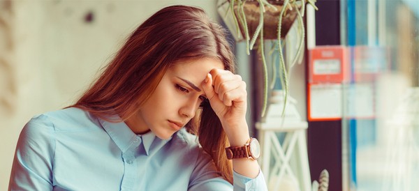 woman sitting at a table looking upset with her hand on her forehead