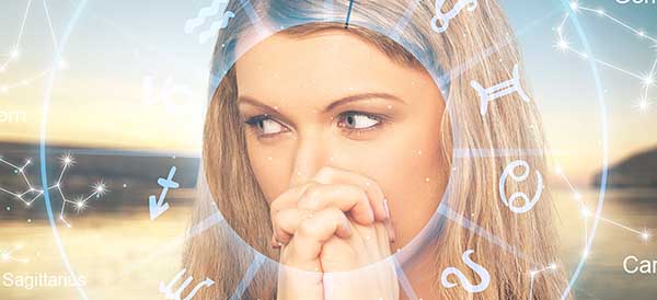 a woman has her hands clasped with surrounding astrology elements