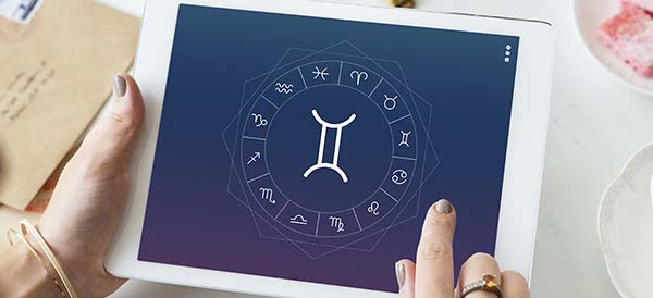 a woman looks at a tablet that has the Gemini zodiac symbol