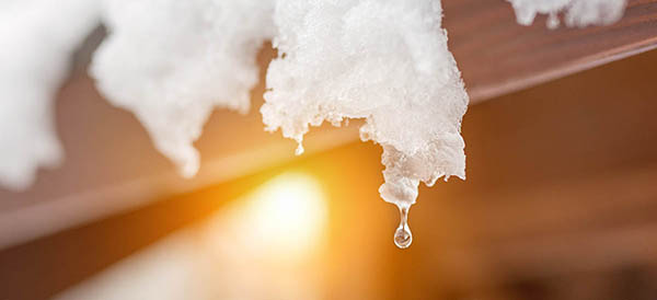 melting snow icicles on roof as a sun shines in the background